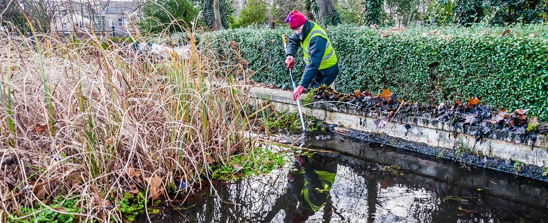 Conservation workers clear leaves, vegetation and silt from the dipping pond, Newham, London, UK By Abdul