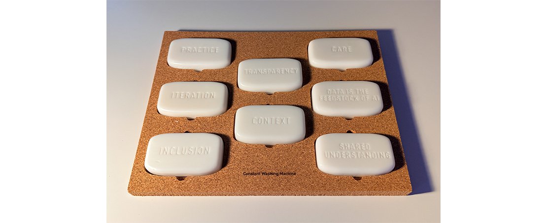 A cork board displaying six neatly arranged soap bars, each with different words or phrases written on them.