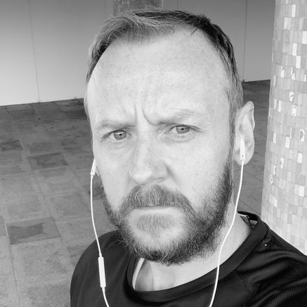 Black and white headshot of Christopher Bancroft facing forward with a tiled backdground.