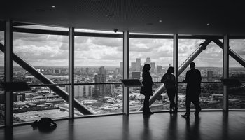 People meeting near large window with city views