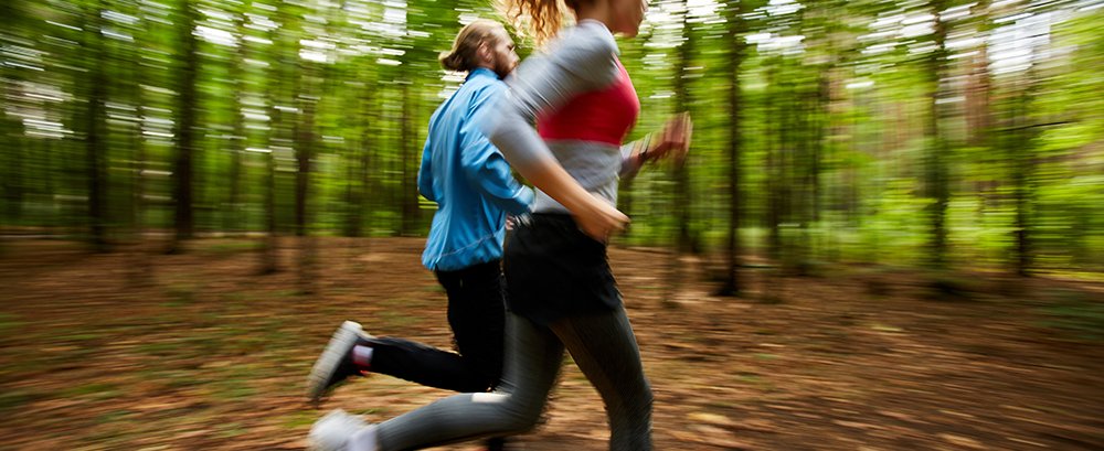 Young couple in activewear running on forest road with blurry trees on background